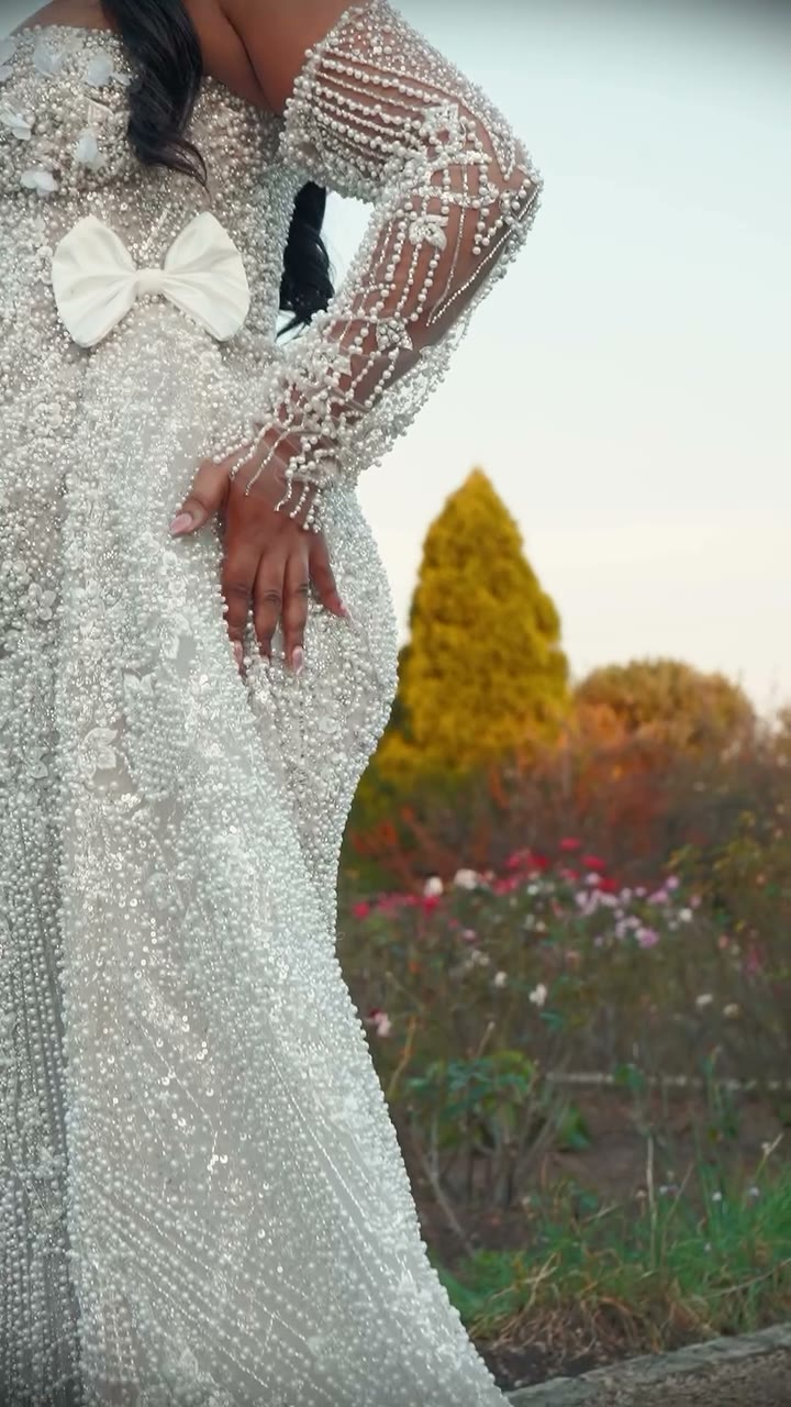 Close detail of a crystal and pearl beaded bridal gown with a white satin bow at the shoulder and a sheer beaded sleeve